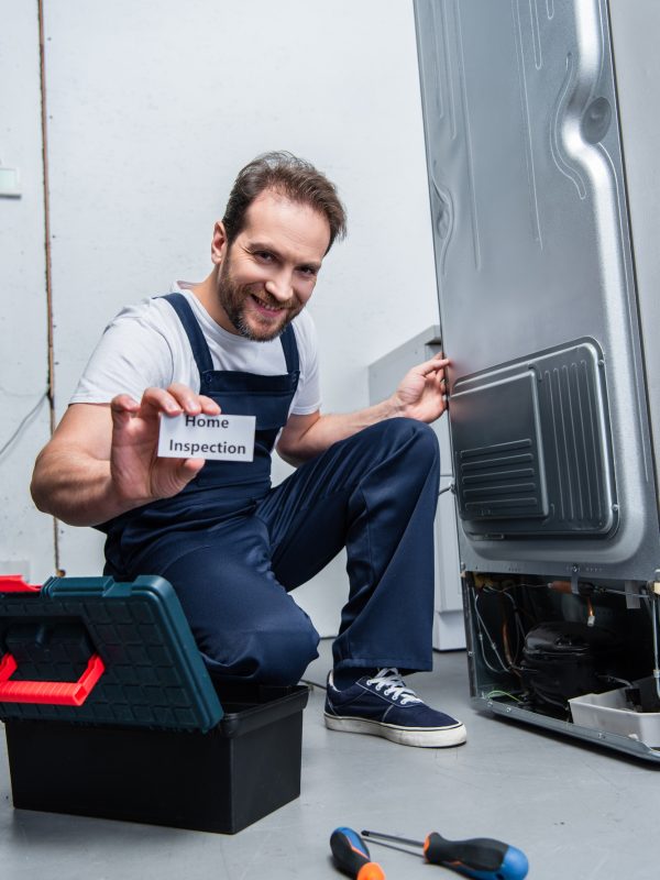smiling adult craftsman showing card with lettering home inspection while sitting near broken