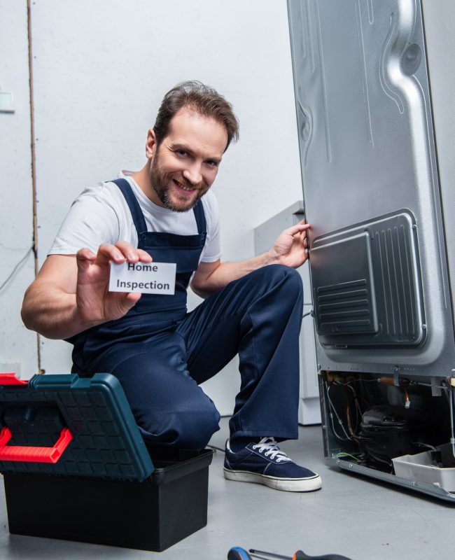smiling adult craftsman showing card with lettering home inspection while sitting near broken